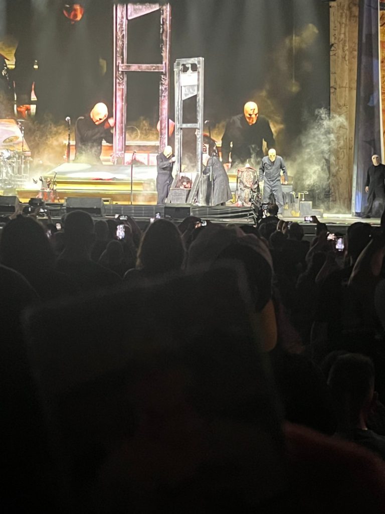 [Image: The Billy Ripken card is held up for the camera as Alice Cooper is prepared for one of his trademark onstage beheadings.]