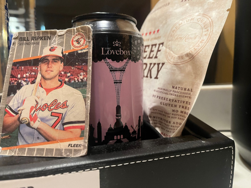 [Image: Billy Ripken card sitting on a hotel minibar offering bagged beef jerky and a soda can shaped "intimacy kit" for purchase.]