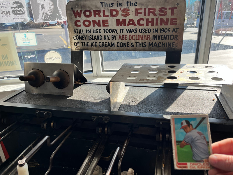 [Image: Cal Ripken card held in front of Abe Doumar's, the inventor of the ice cream cone, original cone making machine from 1905. The machine is still in use today at Doumar's, a drive in diner continuously operated in Norfolk since 1936.]