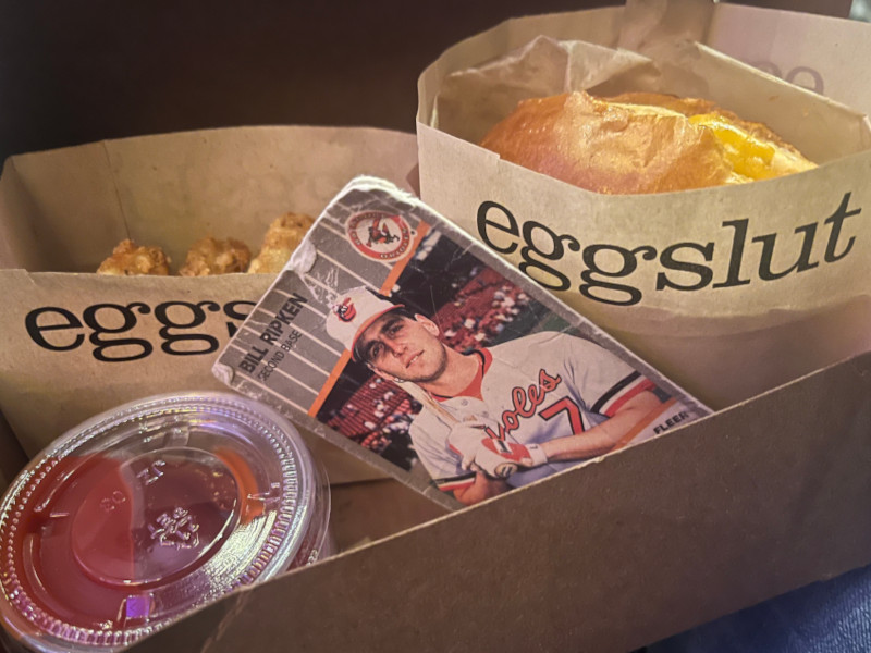 [Image: Billy Ripken card sitting in a box of food from Eggslut. Hash browns and ketchup on the left, a bag containing a Fairfax sandwich on the right.]