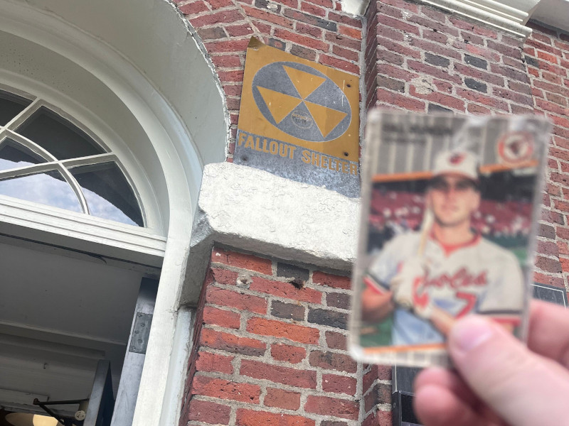 [Image: Closeup shot of the Billy Ripken card at Faneuil Hall next to the building's brickwork and Fallout Shelter placard.]