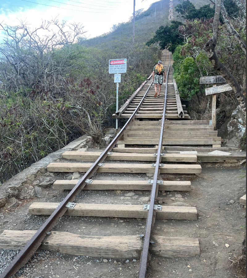 [Image: A man walks across the bridge on the Koko Crater Tramway. A warning sign advising hikers to stay away from the bridge has just been passed.]