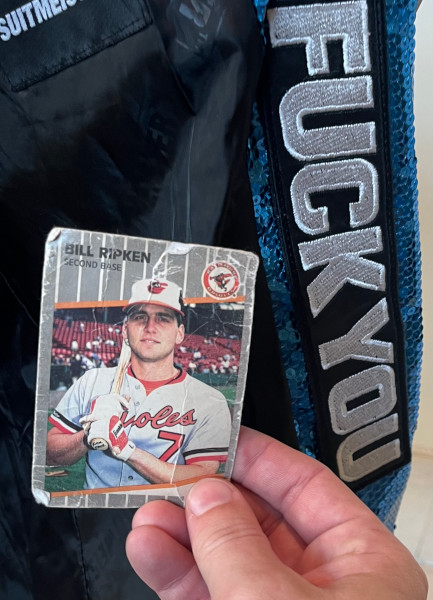 [Image: Billy Ripken card held against the interior of the suit jacket of a person dressed as Papa Emeritus IV. Stitched inside is a large "Fuck You" sign in massive white block letters."]