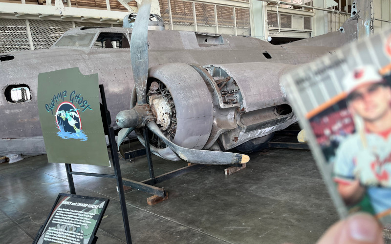 [Image: The Billy Ripken card in front of wrecked B-17 stored in Hangar 79 at Pearl Harbor's Pacific Aviation Museum. The plane shows decades of exposure to the weather. Nicknamed "Swamp Ghost," the plane's inner port engine is visible with the propeller badly bent backwards by the impact of crash landing in a swamp.]
