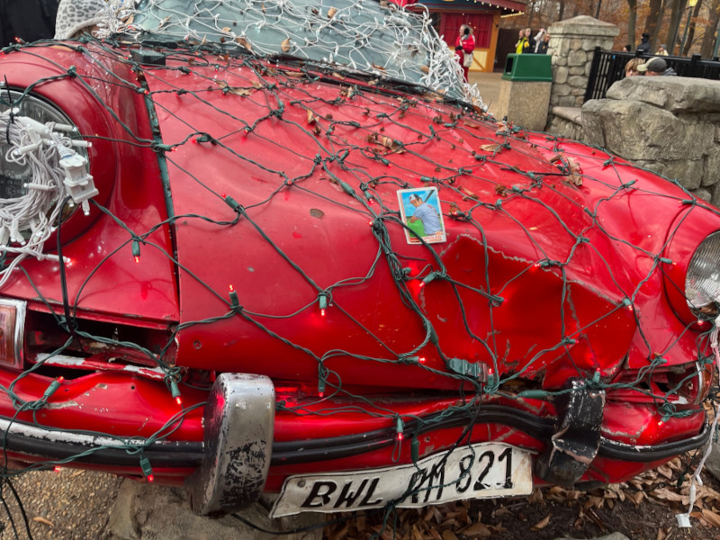 [Image: Front view of a wrecked 1970s Porsche 911. The front is heavily dented and looks like it hit a pole. The car is decorated for Christmas with a large number of Christmas lights. A 1982 Cal Ripken rookie card is tucked into the light strings.]