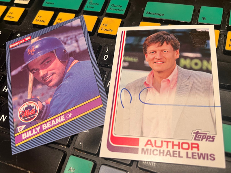 Image: 1986 Donruss Billy Beane and 2018 Topps Fan Favorites Michael Lewis baseball cards laying across a Bloomberg Terminal keyboard.