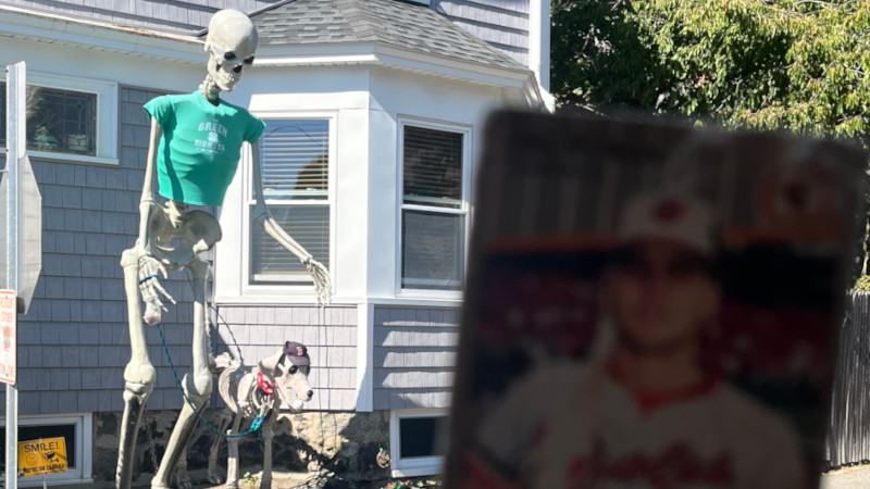 [Image: The Billy Ripken card is held up in front a house decorated for Halloween. A 12-foot tall skeleton is walking a skeleton dog. The dog is wearing a Boston Red Sox cap and the skeleton is wearing a green t-shirt that reads "Green Monsta"]